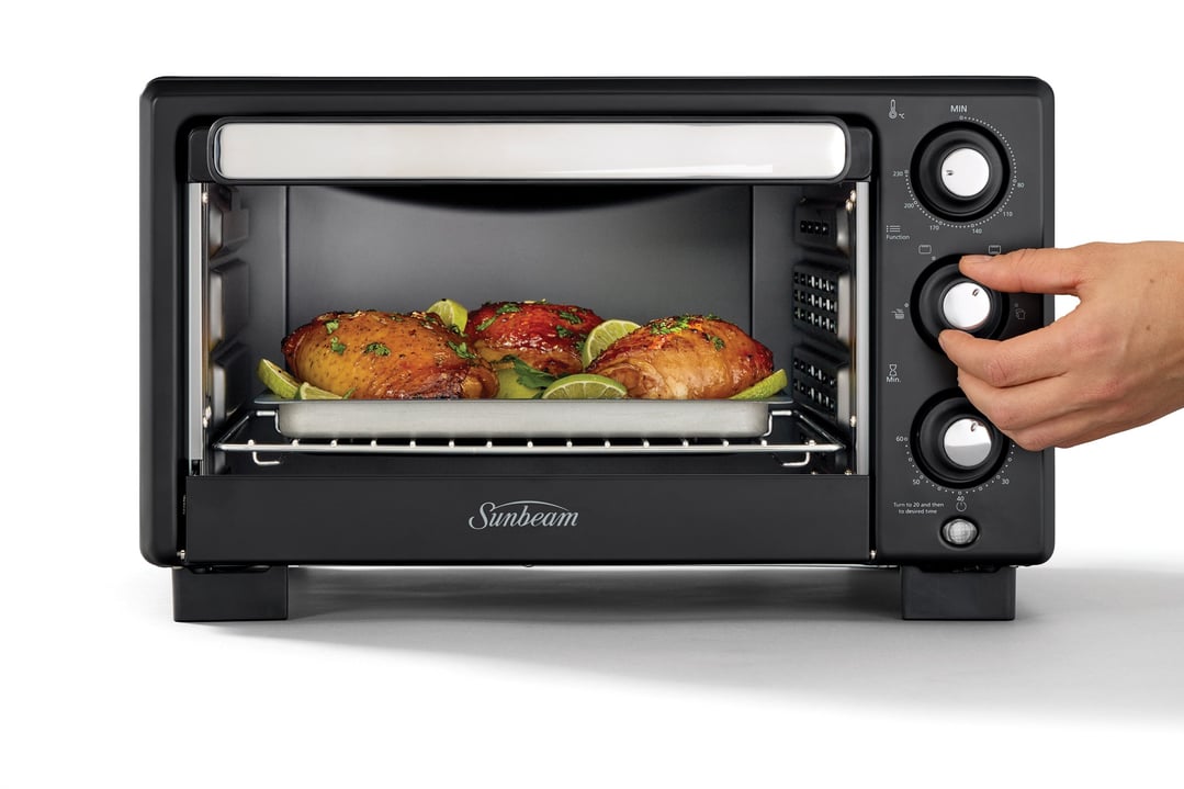 Hand adjusting controls on a black Sunbeam air fryer oven with food inside