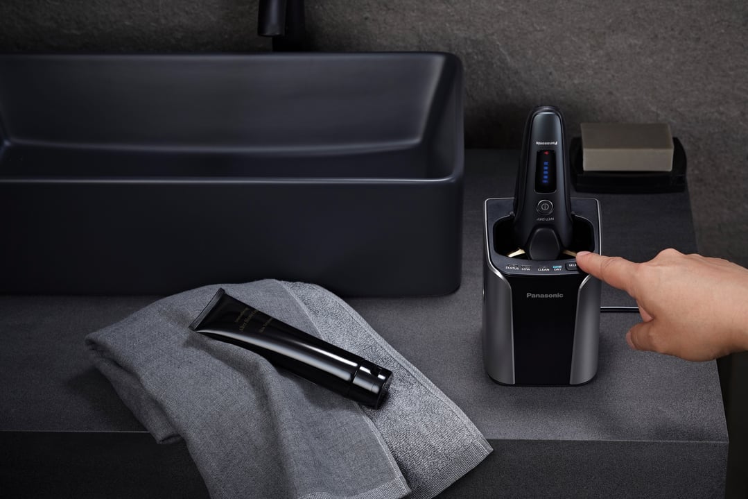 Hand pressing button on Panasonic shaver in charging dock on bathroom counter