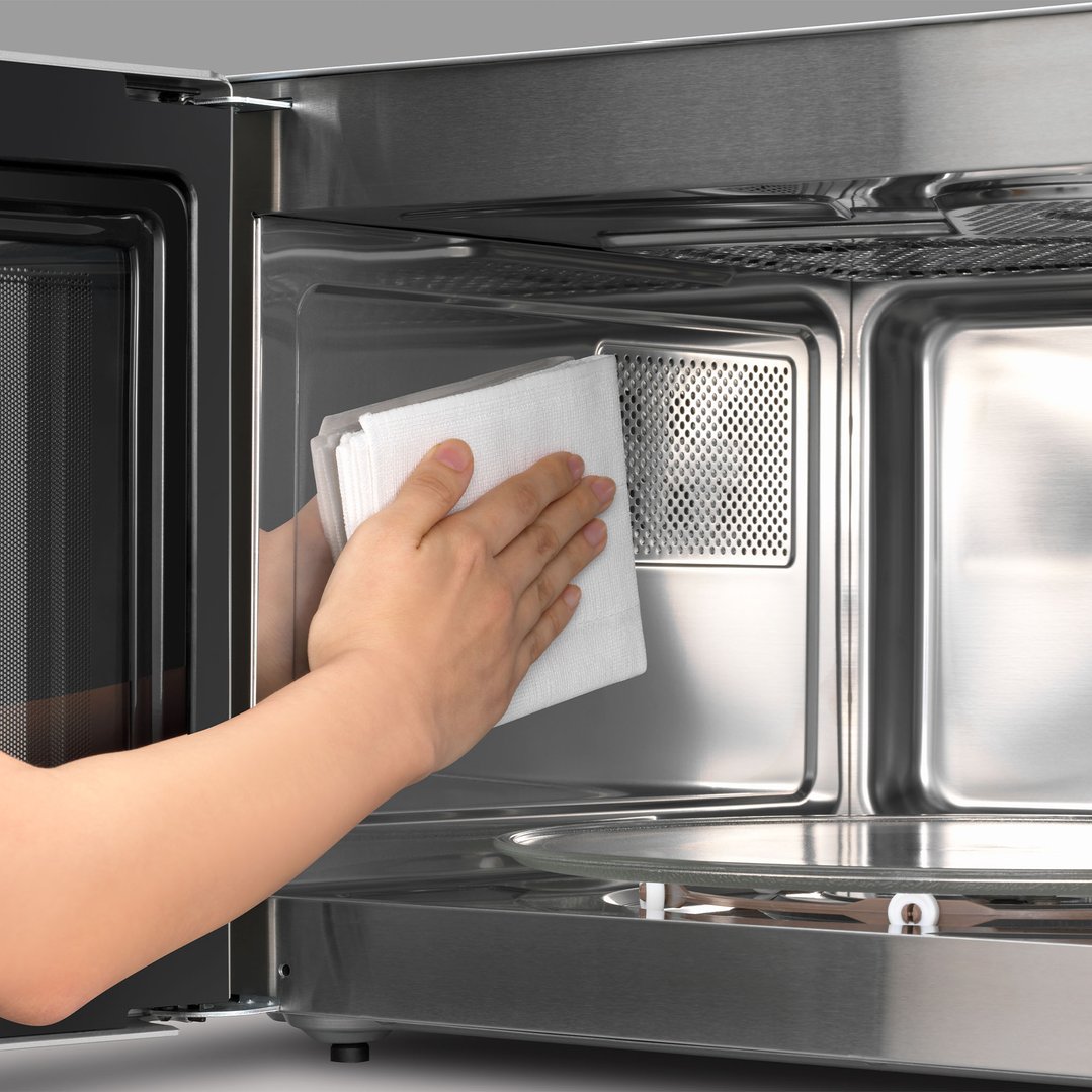Hand cleaning the interior of a microwave oven with a white cloth
