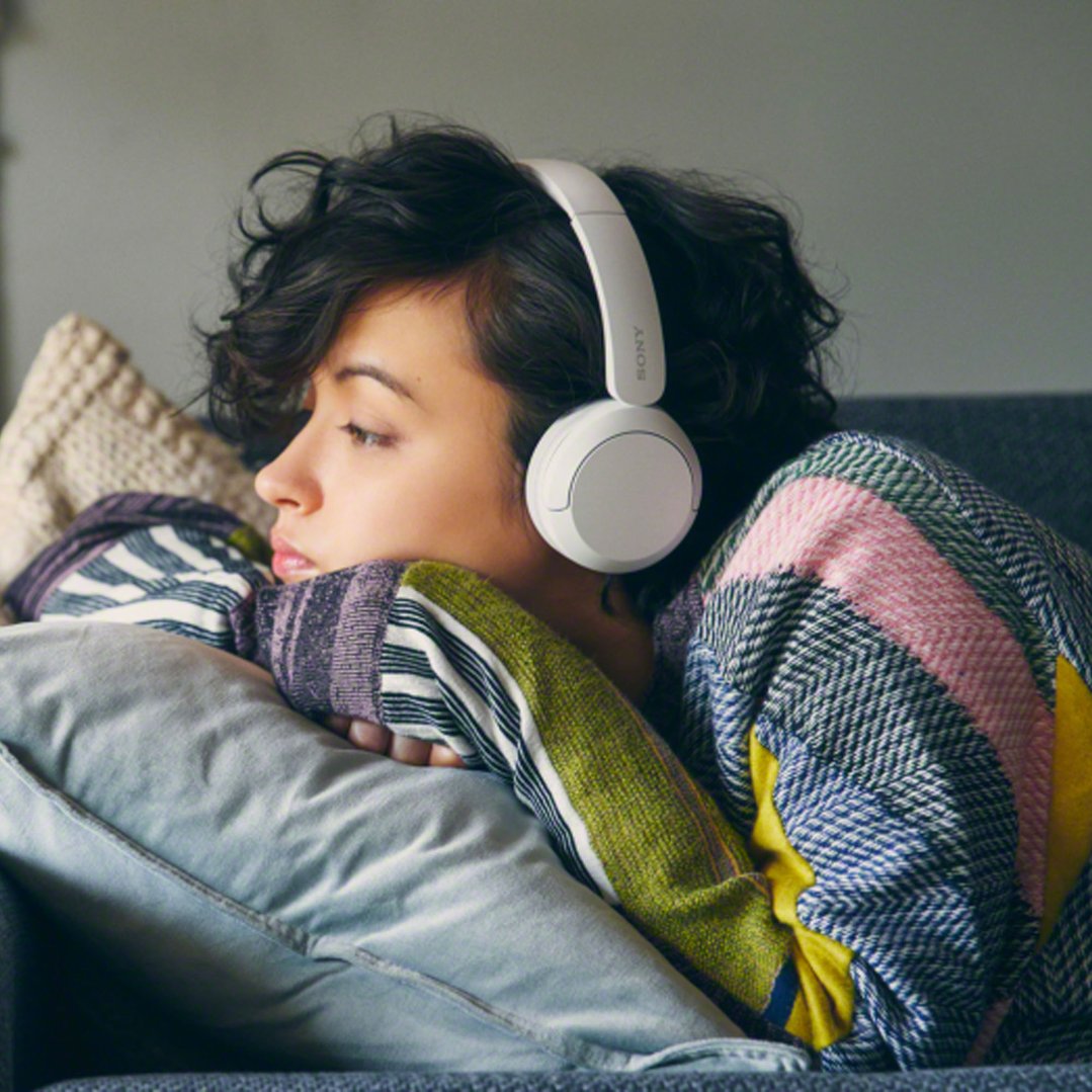 Woman wearing white Sony Wireless Headphones, resting on a pillow on a couch