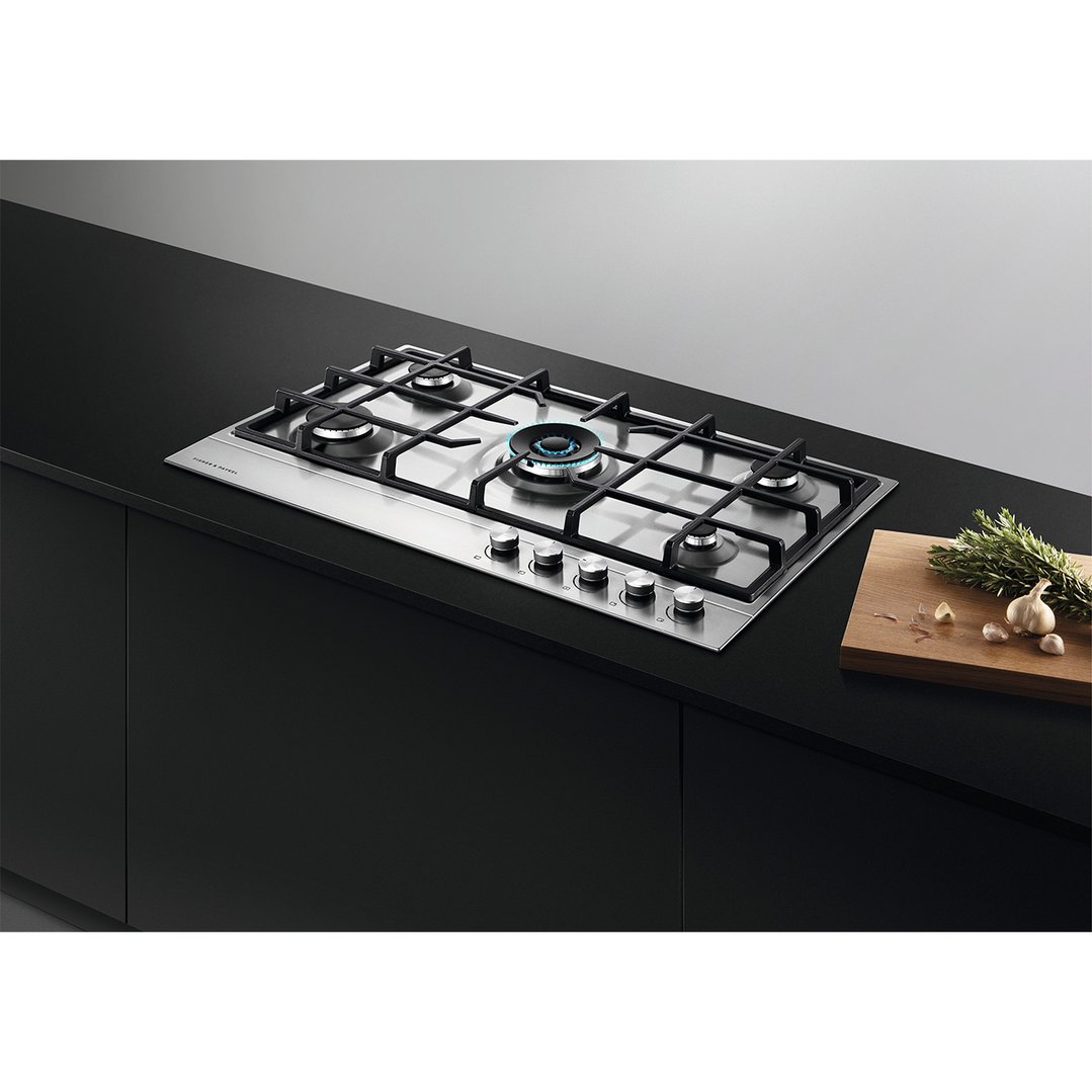 Stainless steel gas cooktop with five burners built into a black kitchen counter