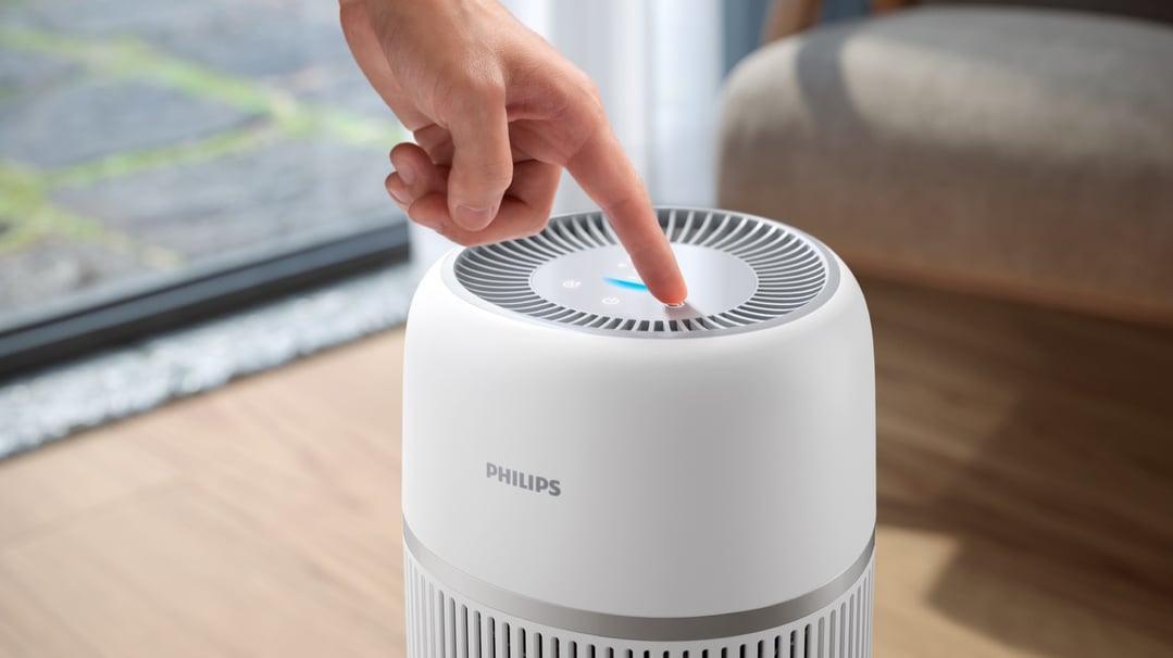 Hand pressing the power button on a Philips Air Humidifier in a room