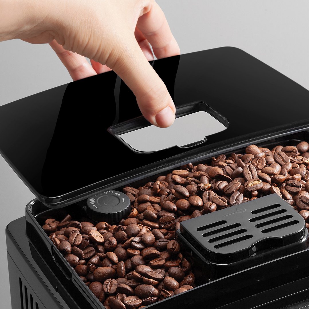 Hand opening the lid of a coffee machine filled with coffee beans