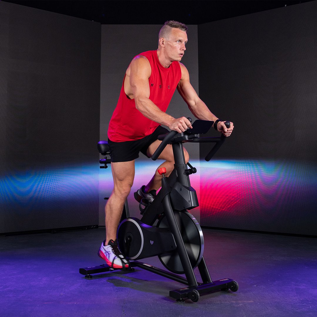 Man in red tank top and black shorts riding a spin bike