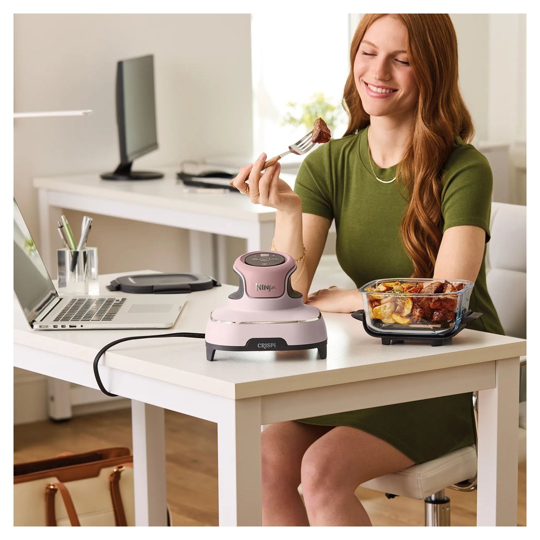 Woman eating food from a glass container next to a pink Ninja air fryer