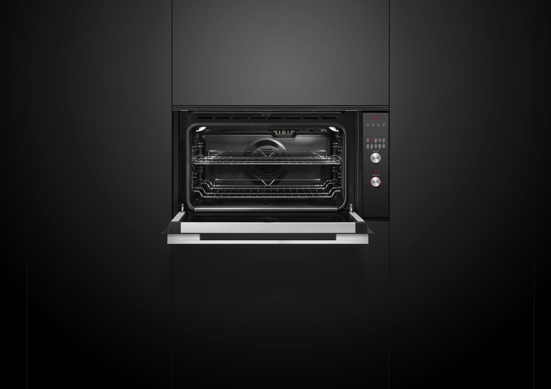 Black built-in oven with door slightly ajar in a dark kitchen
