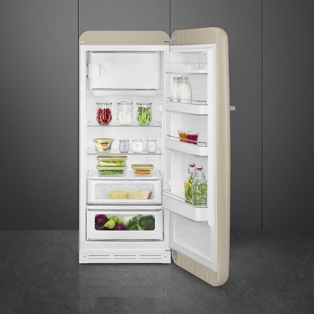 Open pale beige SMEG refrigerator filled with food in a dark room
