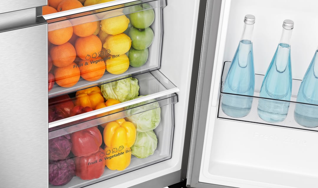 Open fridge interior showing fruit and vegetable drawers and water bottles on shelf