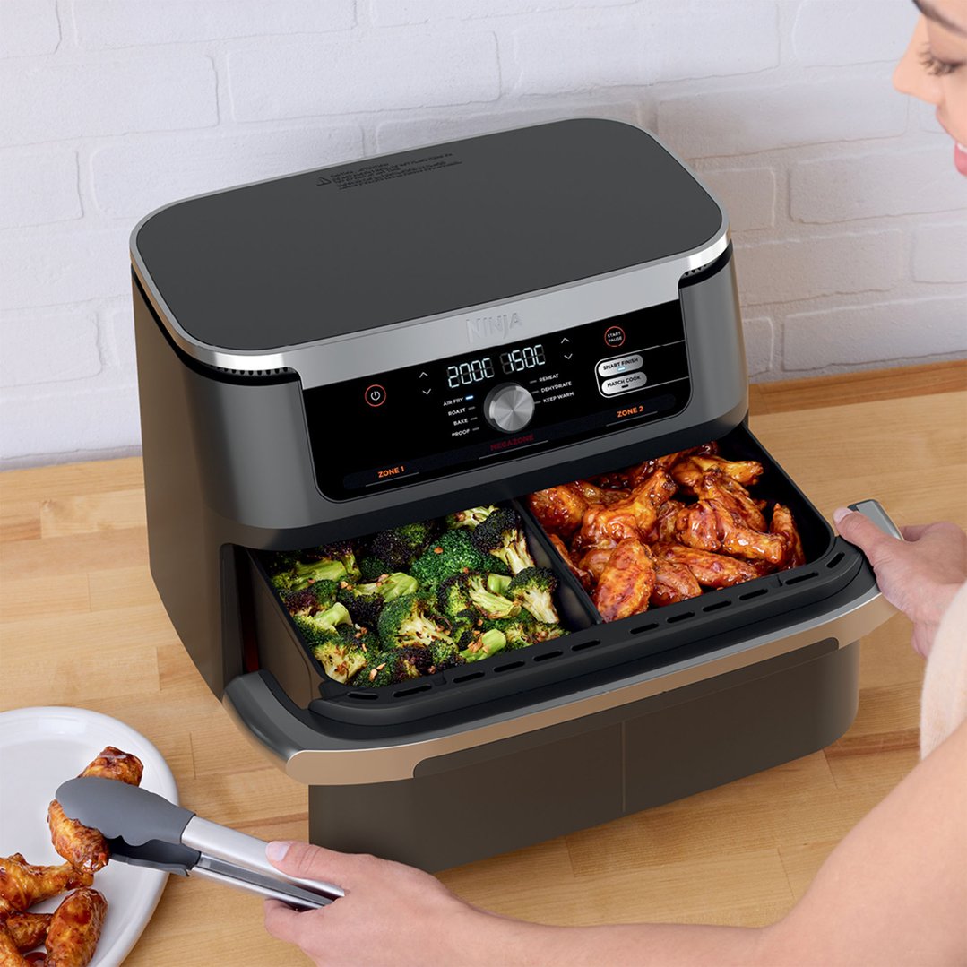 Woman using tongs to remove chicken wings from the air fryer