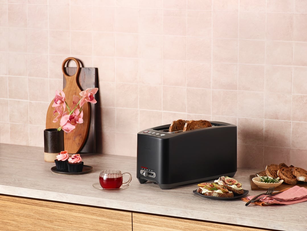 Black Breville toaster with toast on a kitchen counter with food and flowers