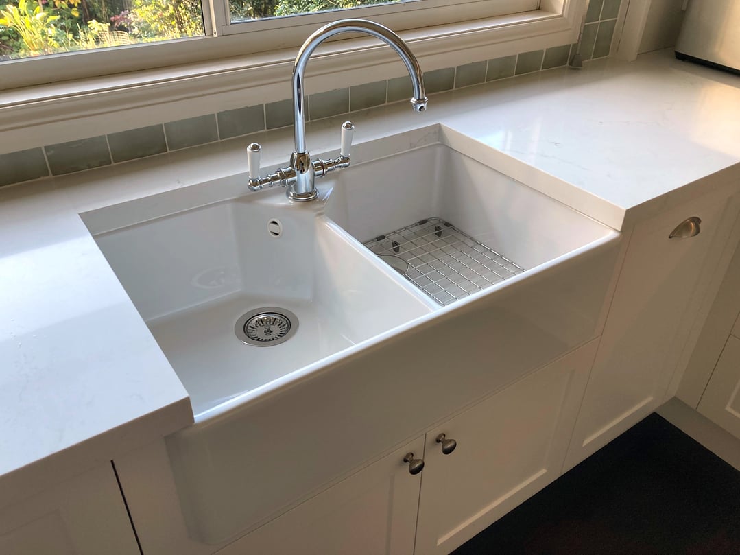 A white double-basin sink with a chrome faucet and a stainless steel grid