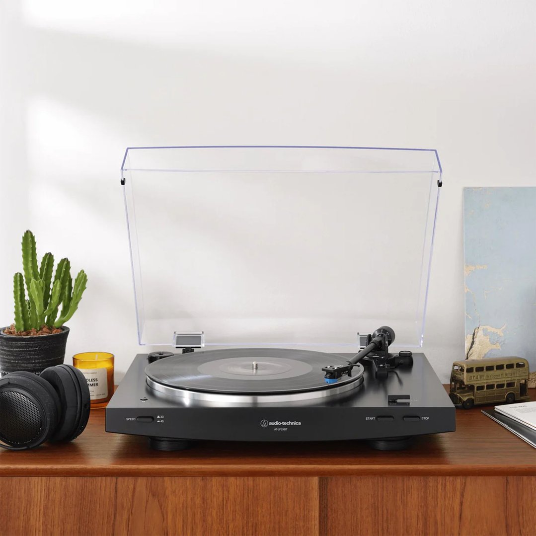 Black Audio-Technica turntable on a wooden cabinet with headphones and plants