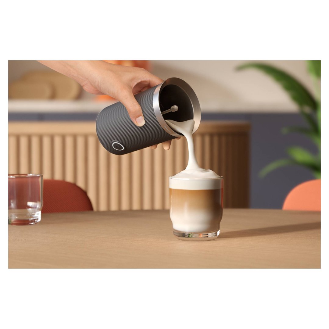 Hand pouring frothed milk from a Philips milk frother into a glass of latte