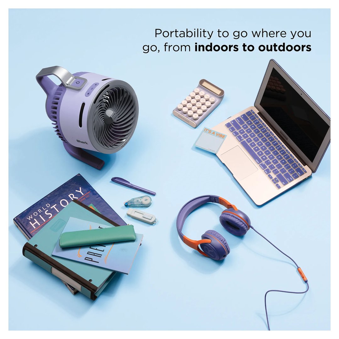 Lilac portable fan on a blue surface with school supplies and a laptop