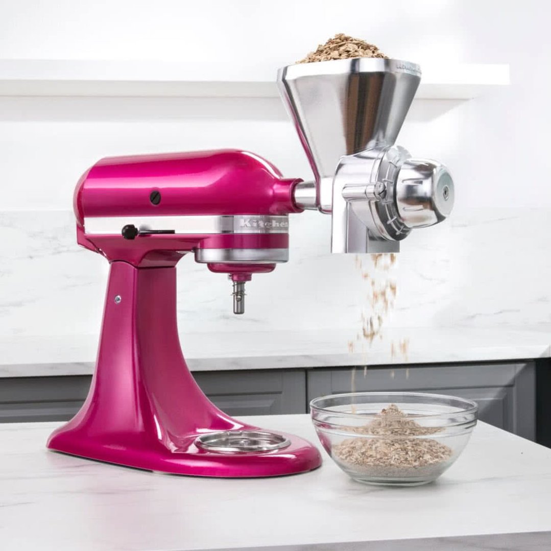 Pink KitchenAid stand mixer with grain mill attachment grinding grain into a bowl