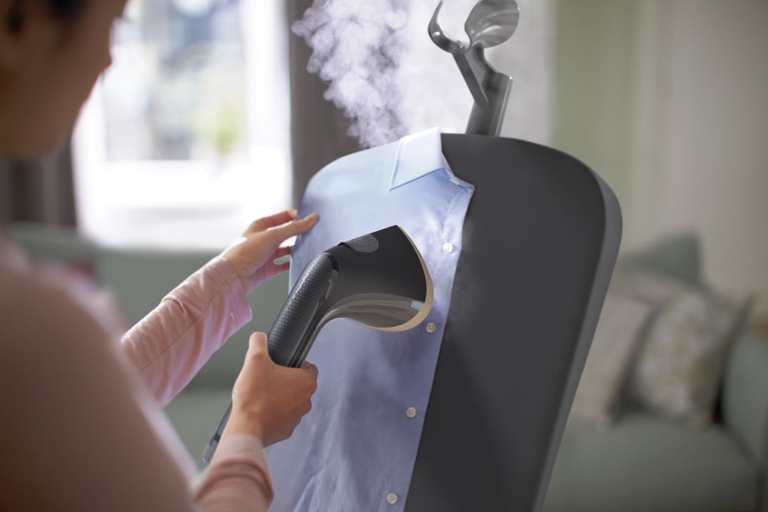 Person steaming a light blue shirt on a garment steamer in a living room