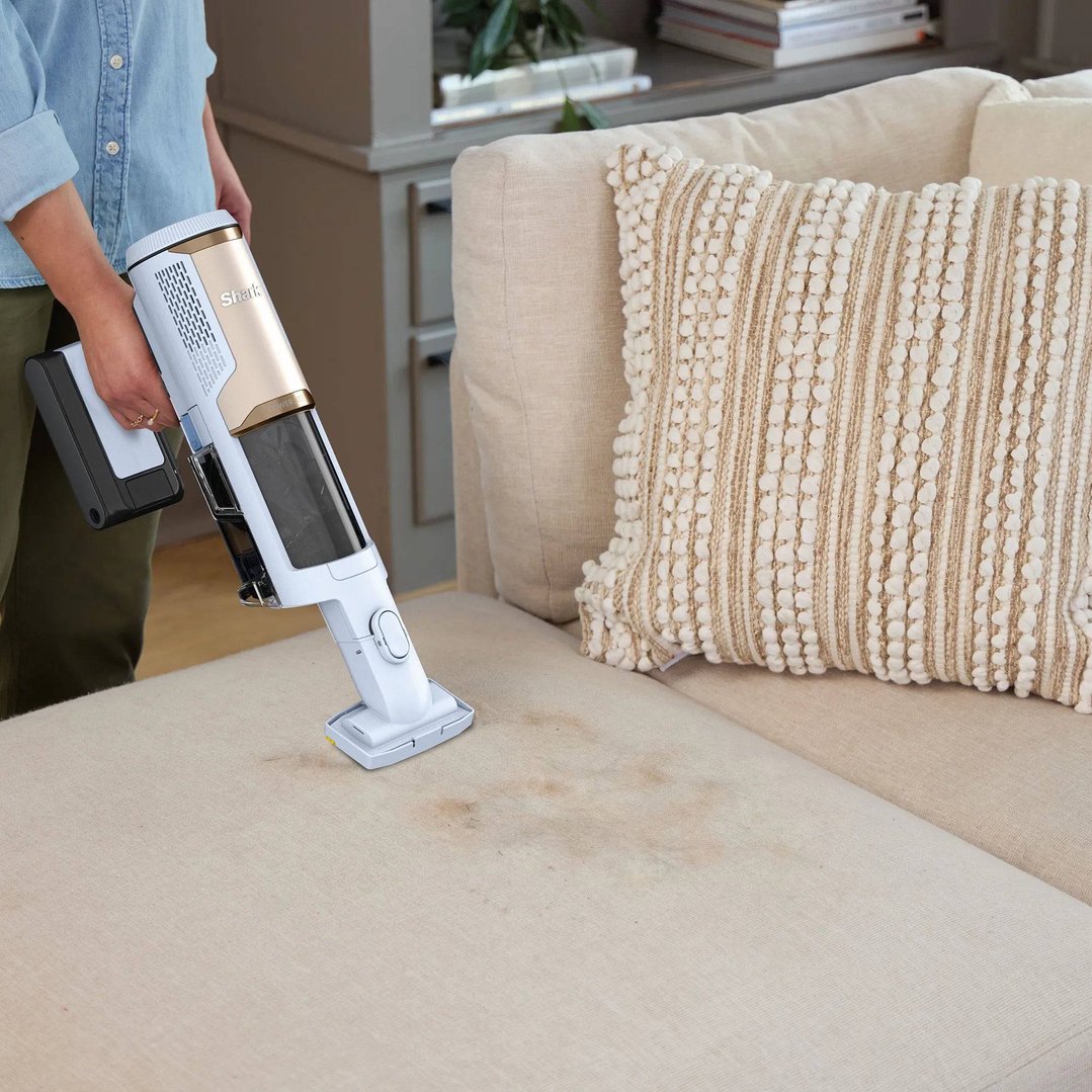 Person cleaning a stained couch with a Shark PowerLite handStickVacuum