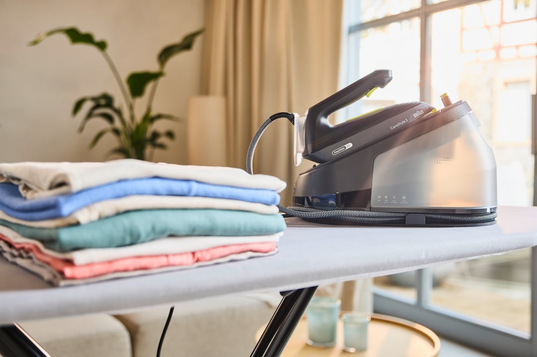 Braun CareStyle 3 steam generator iron on an ironing board with folded laundry