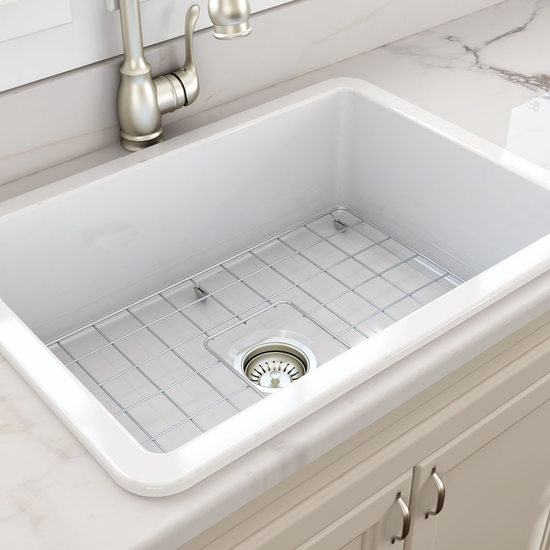 White fireclay sink with a metal grid and faucet in a kitchen setting