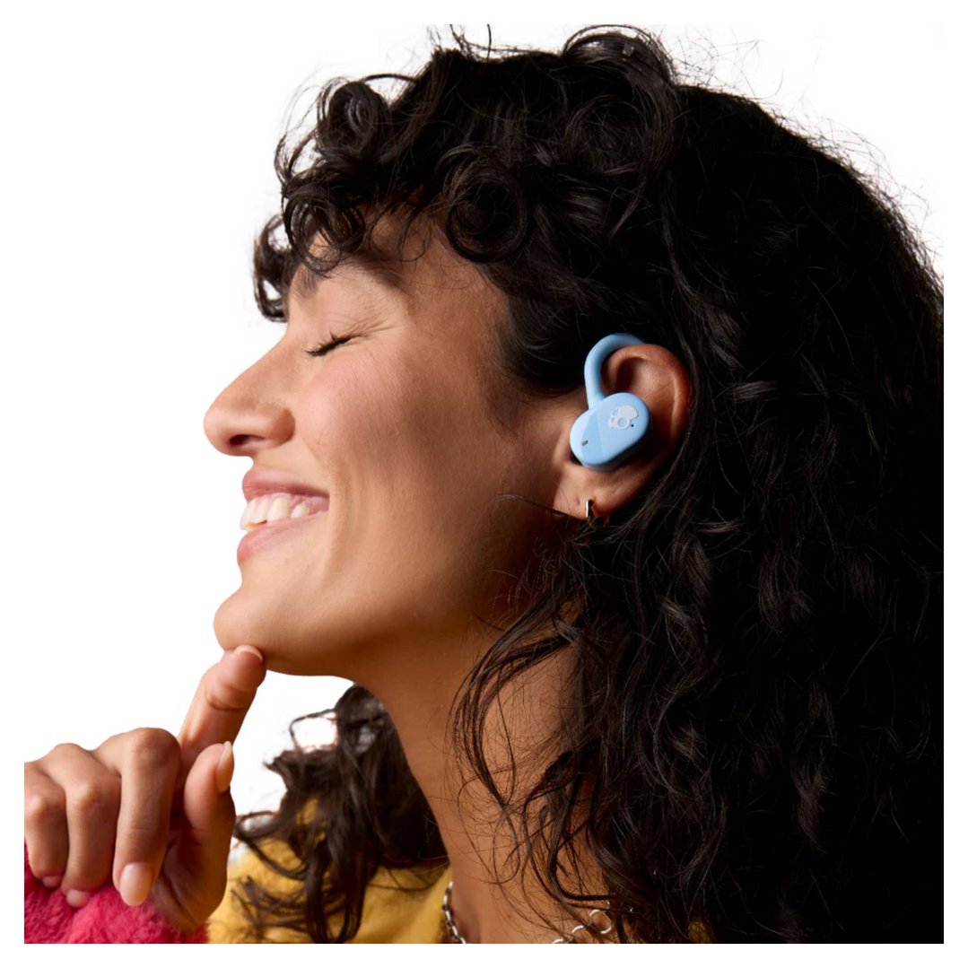 Woman with curly hair wearing a light blue Skullcandy headset in her ear