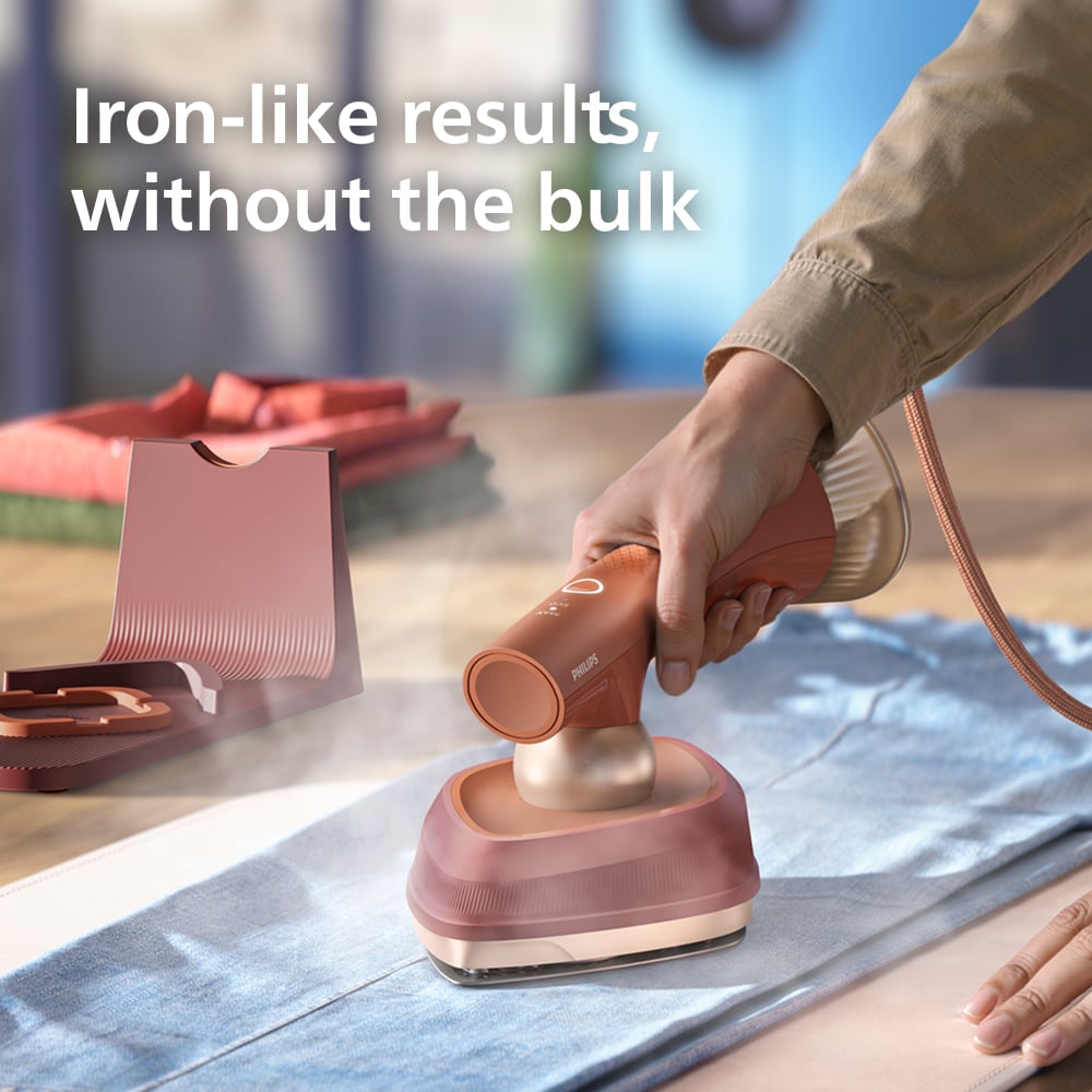 Hand holding a Philips OneTurn Hybrid Iron & Steamer on a light blue garment