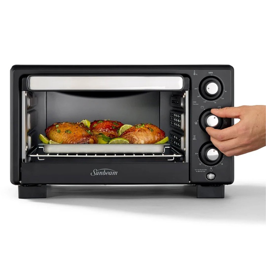 Hand adjusting controls on a black air fryer oven with food inside