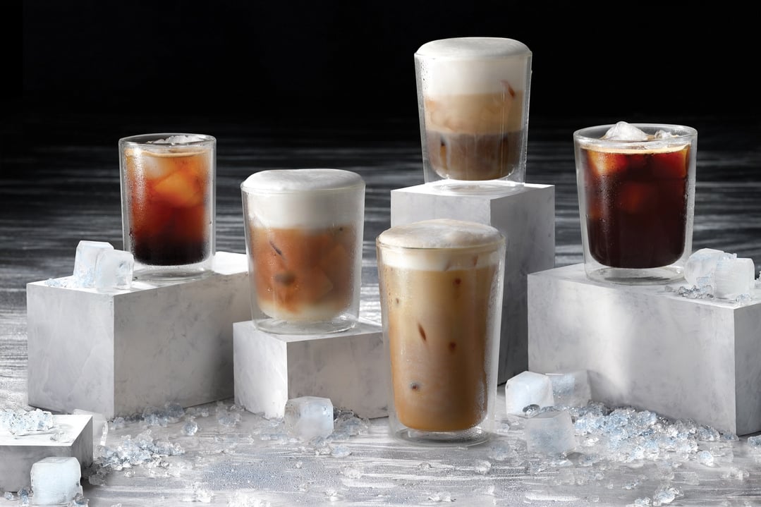 Five iced coffee drinks on white blocks with ice on a dark background