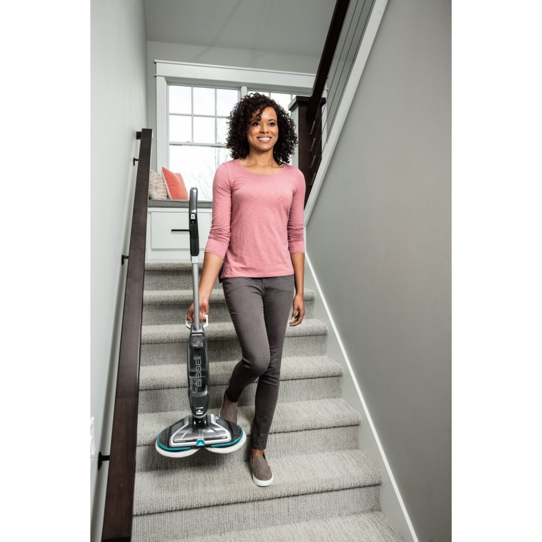 Woman carrying a BISSELL SpinWave Cordless steamMop down carpeted stairs