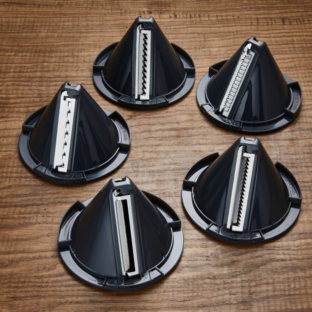 Five spiralizer attachments with different blades on a wooden surface