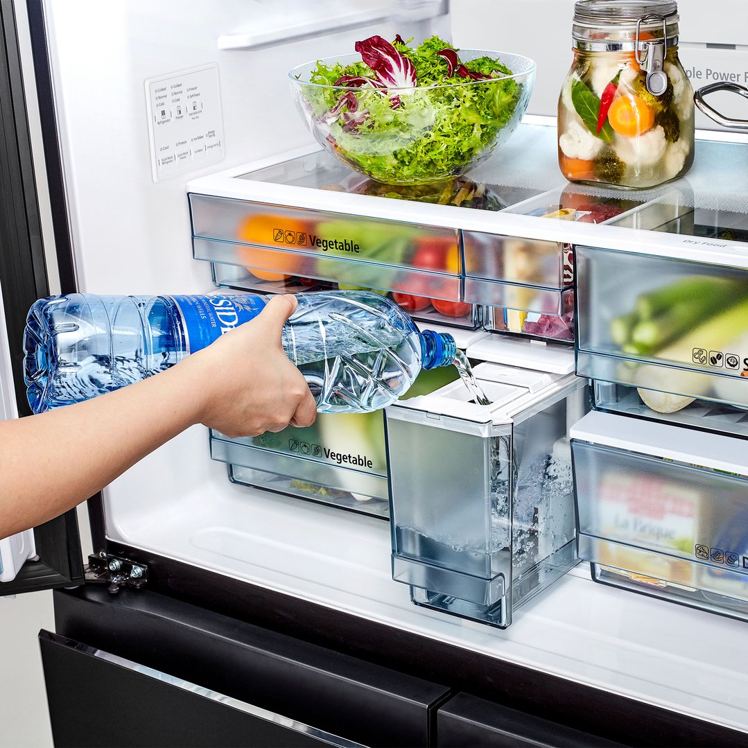 Hand pouring water from a bottle into the ice maker of a Hitachi fridge