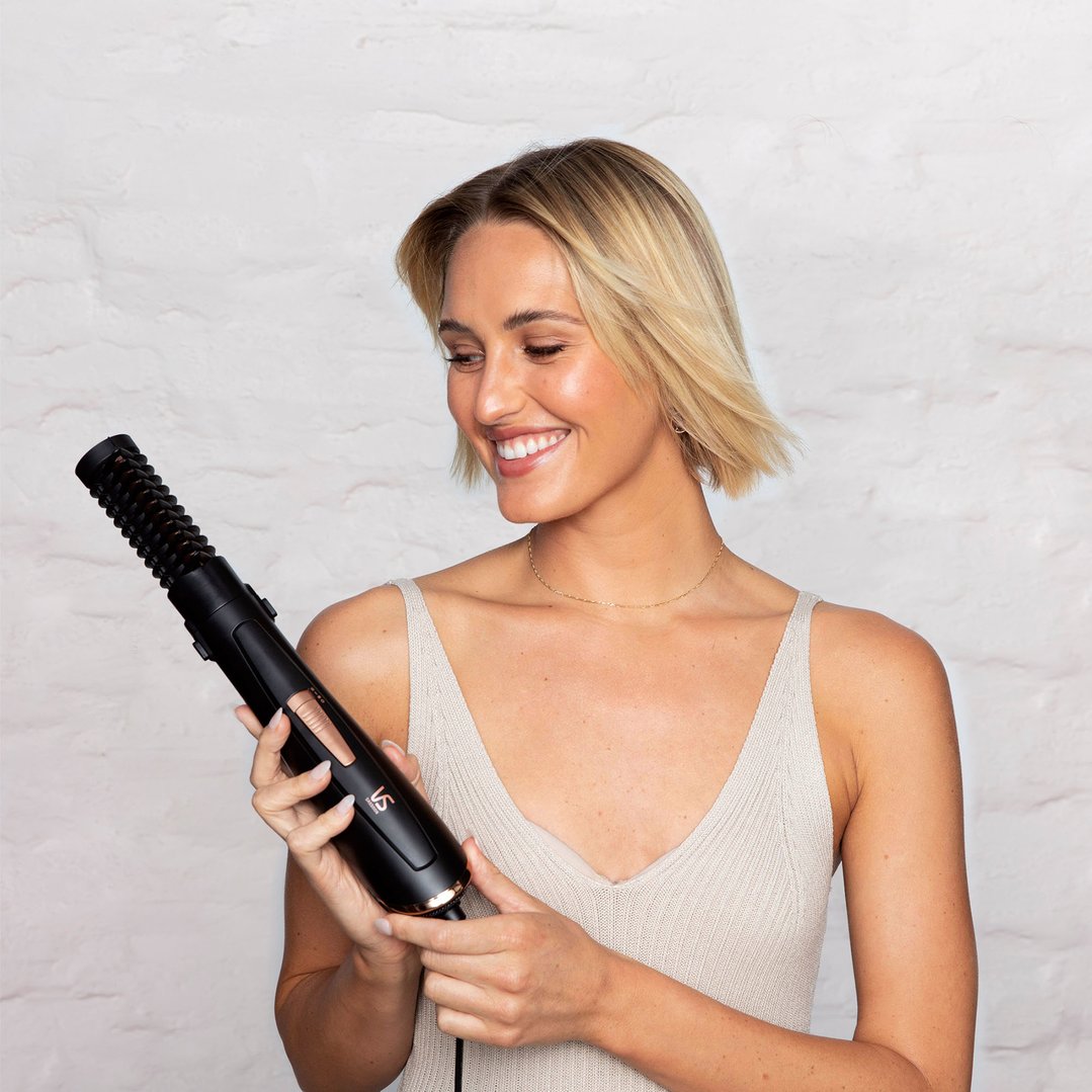 Woman smiling while holding a black VS SASSOON Air Style Brilliance 7-in-1