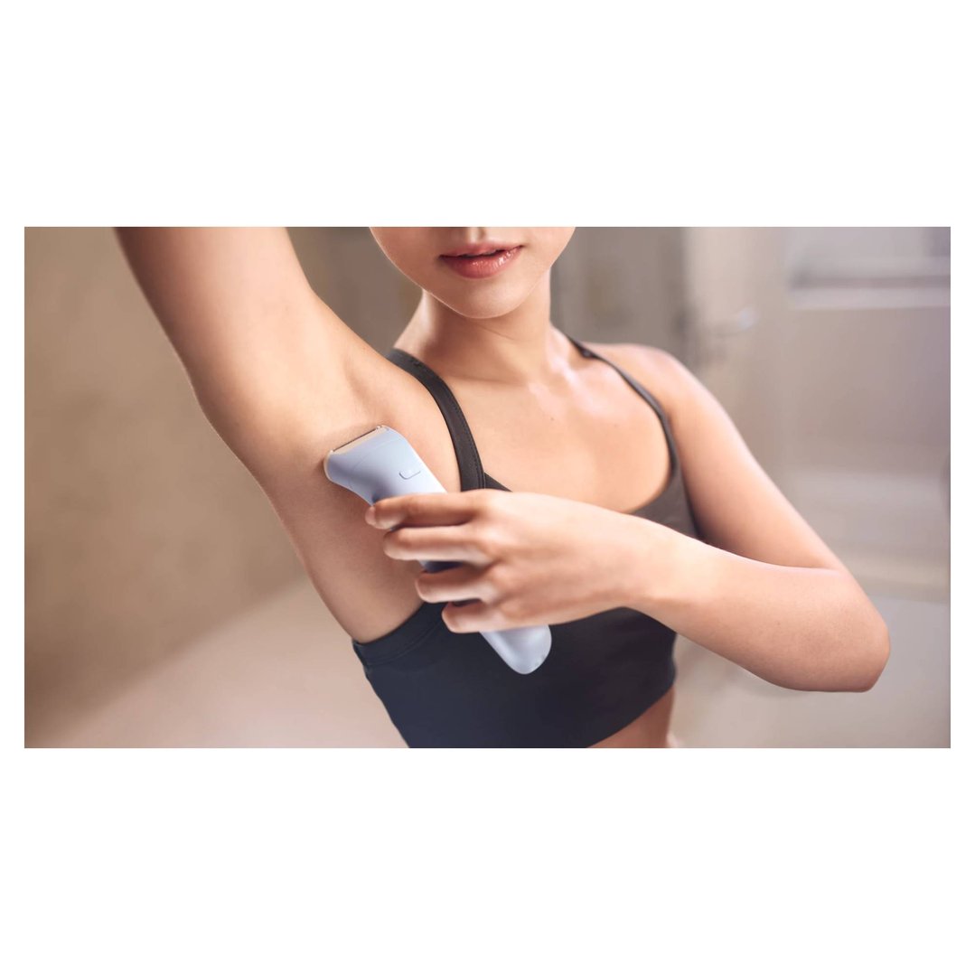 Woman using a PHILIPS epilator on her underarm in a bathroom setting