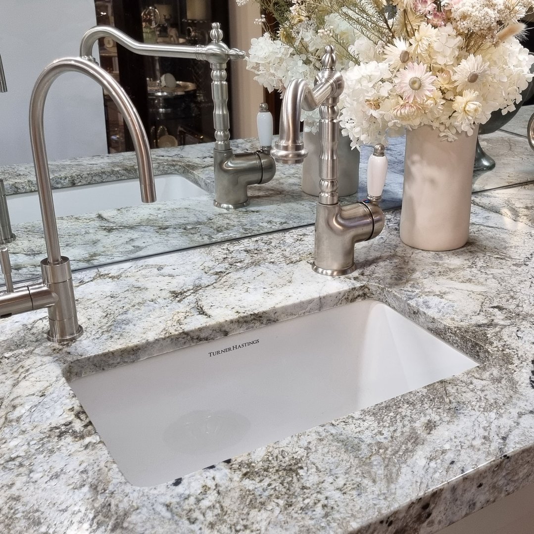 White fireclay sink with two faucets in a granite countertop