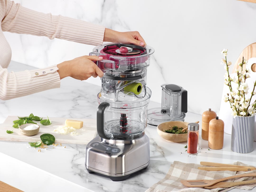 Hands operating a Breville food processor on a marble countertop with ingredients