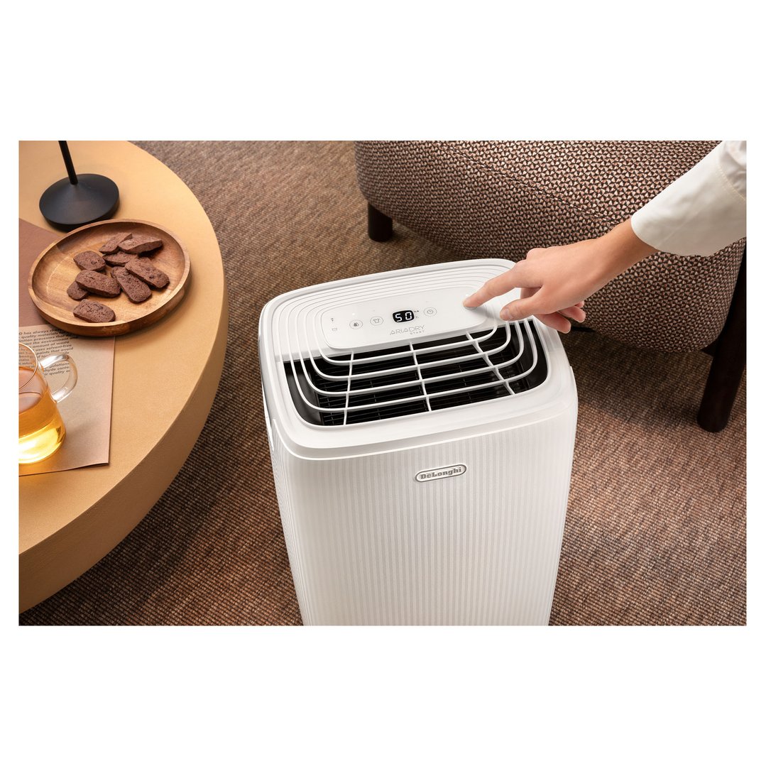 Hand adjusting settings on a white De'Longhi dehumidifier in a living room setting
