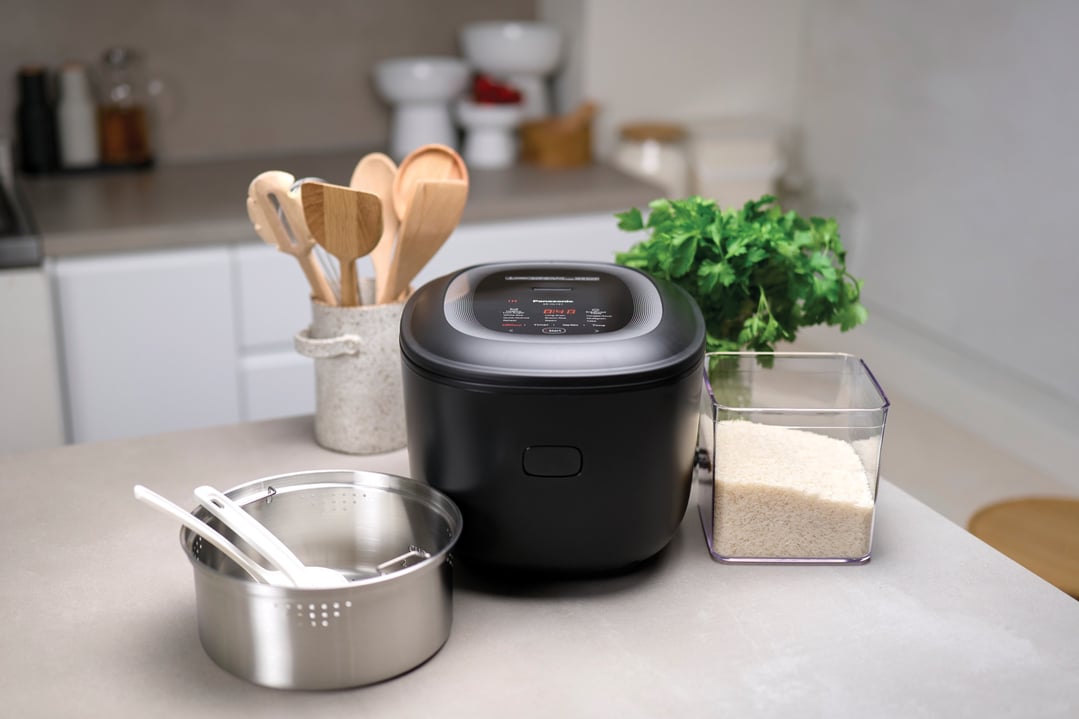 Black Panasonic rice cooker on a kitchen counter with rice and utensils