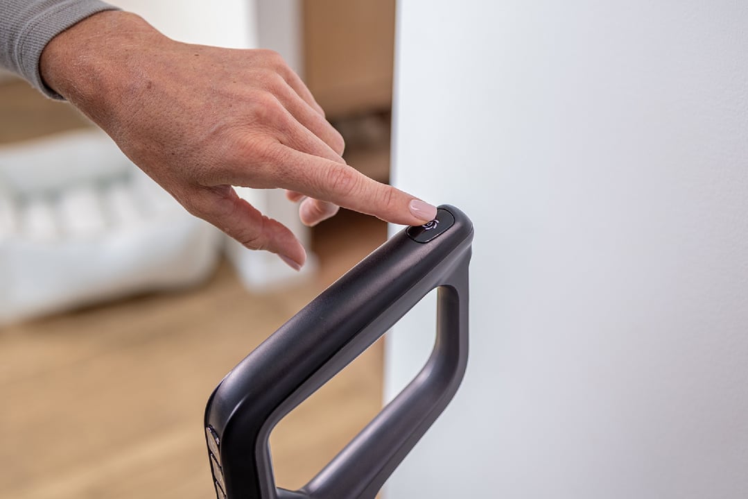 A hand pressing the power button on a BISSELL handStickVacuum