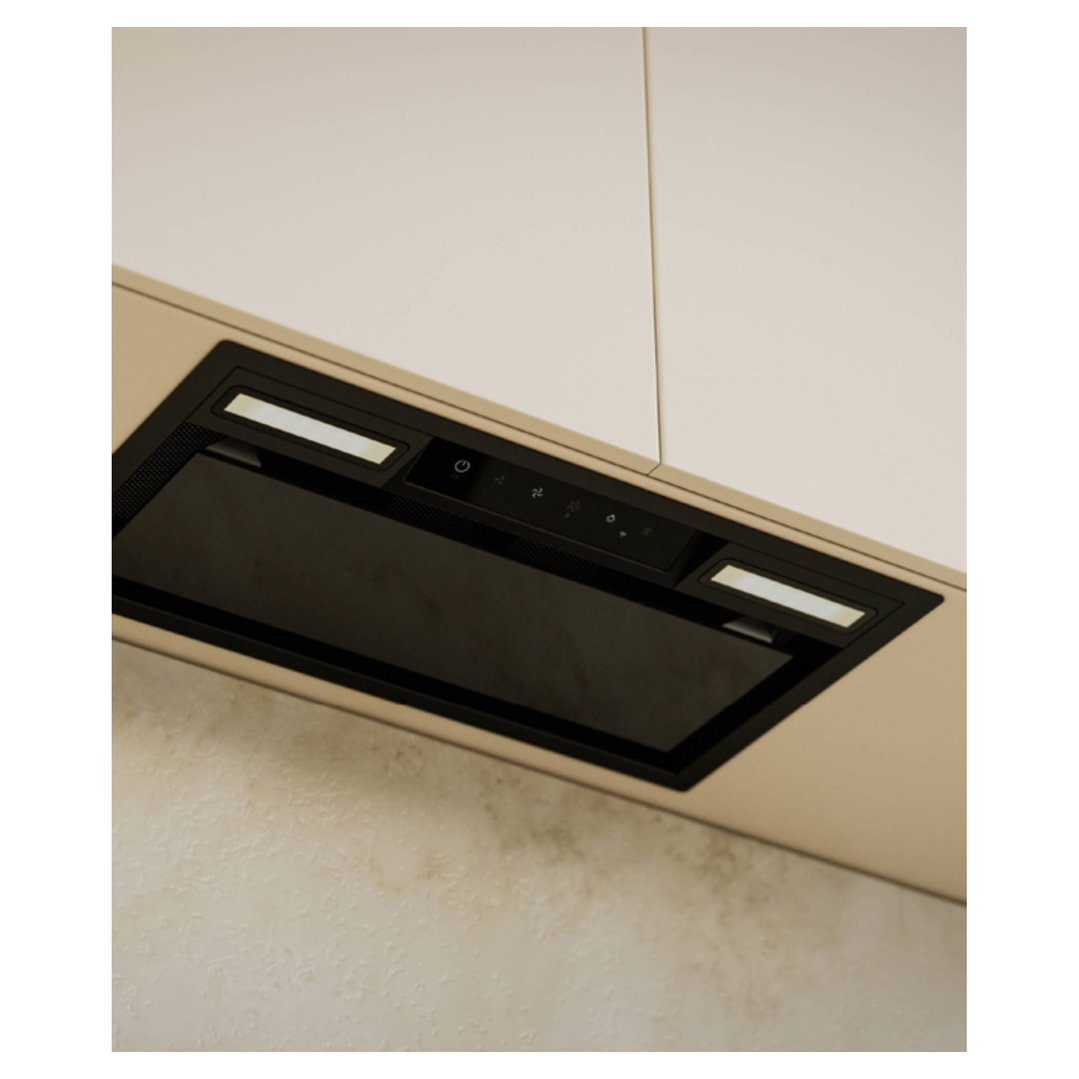 A black integrated rangehood with controls and lights installed under a white cabinet