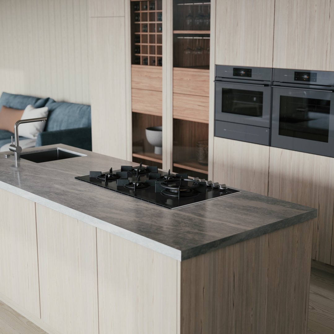 Black gas cooktop on a kitchen island with a sink and ovens in the background