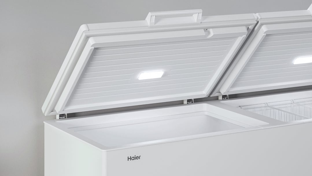 Open white chest freezer with interior light on, showing two compartments