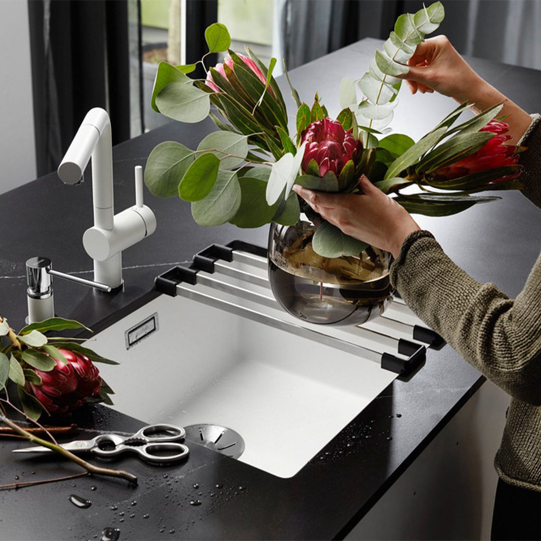 Hands arranging flowers in a vase on a white BLANCO single bowl undermount sink
