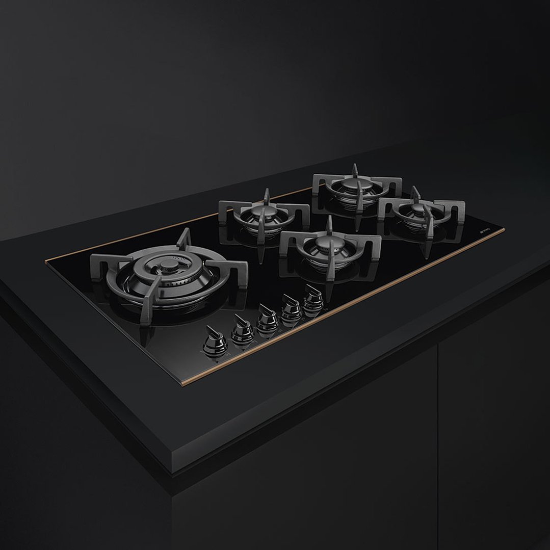 Black 5-burner gas cooktop with gold trim in a dark kitchen setting