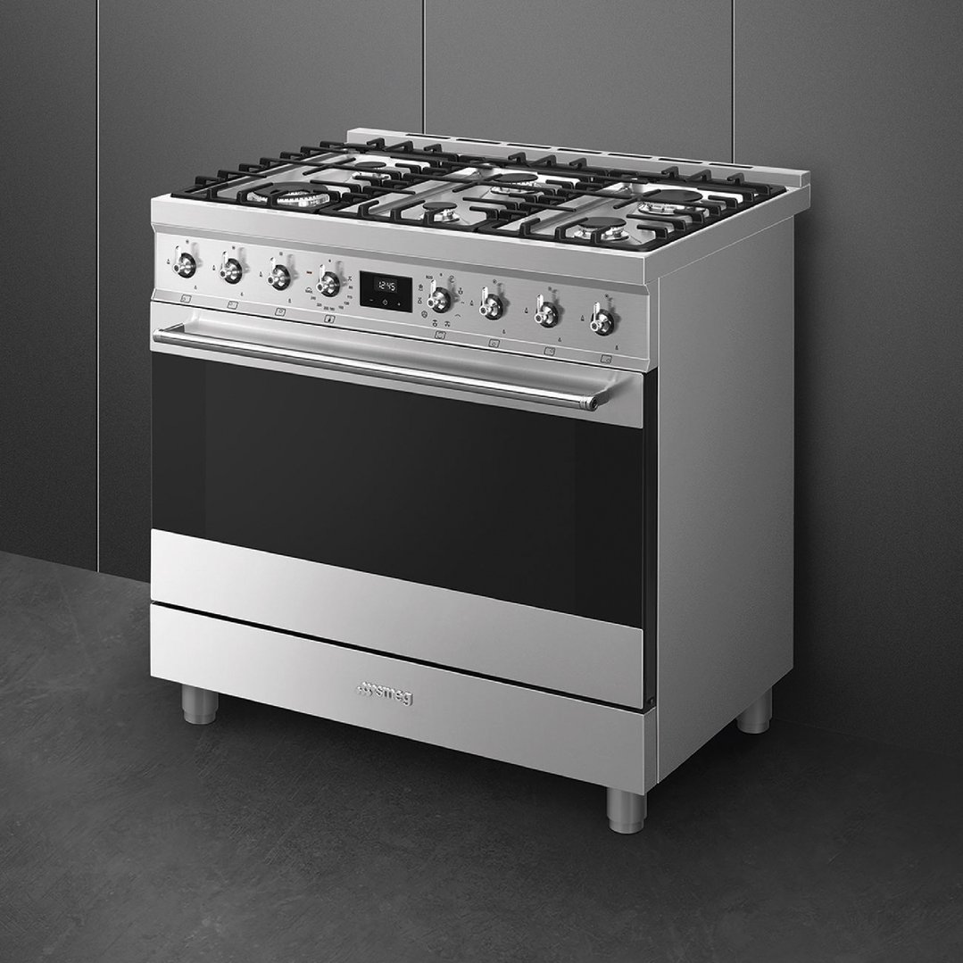 Stainless steel freestanding cooker with gas hob and oven in a dark kitchen setting