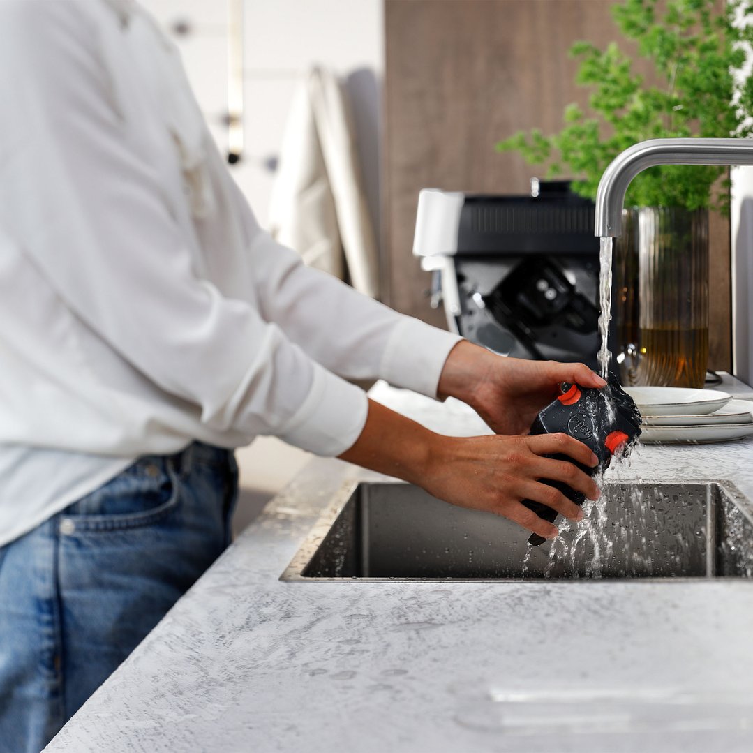 Person rinsing a component of a coffee machine under a kitchen faucet