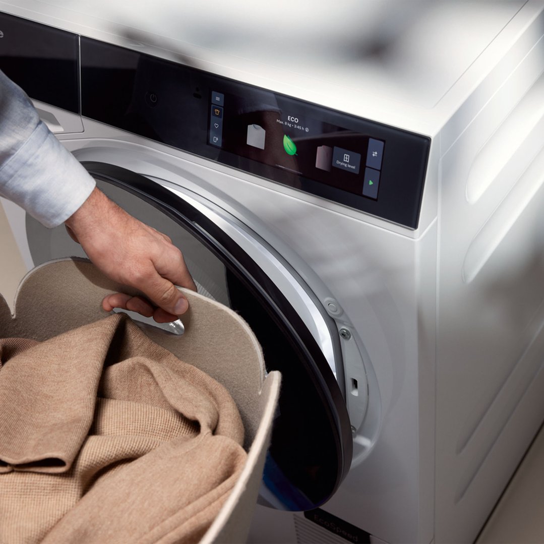 Man loading laundry into the front load washing machine with an open door