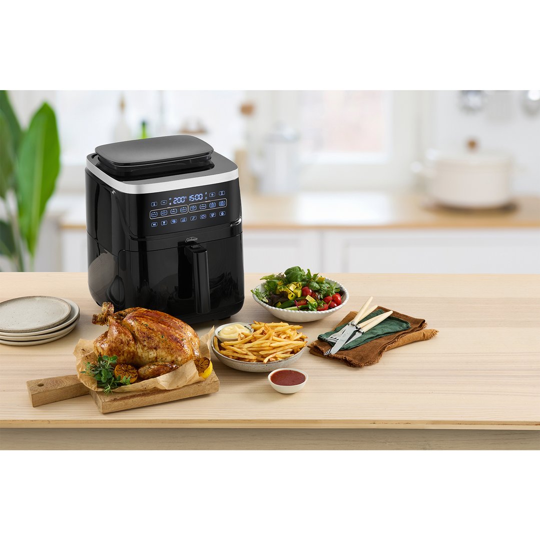 Black Sunbeam SteamFry Air Fryer on a wooden table with a roasted chicken and sides