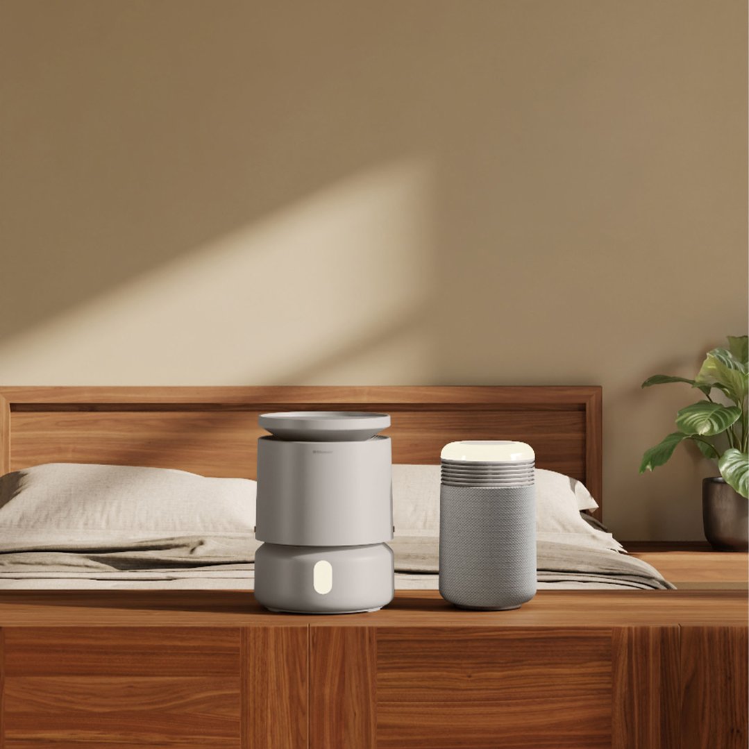 A beige air purifier and a gray speaker on a wooden bed frame in a bedroom