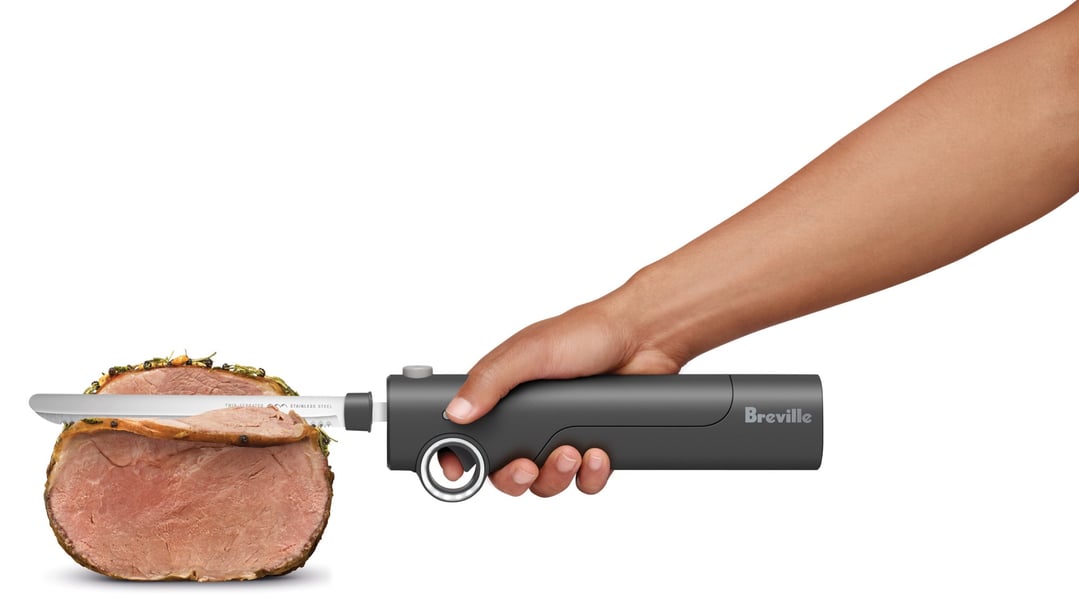 Hand holding a Breville electric knife slicing a roasted meat joint