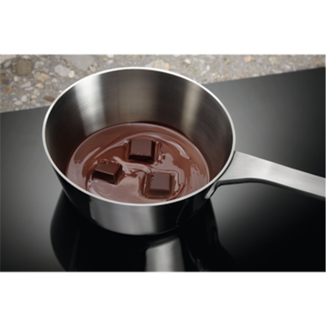 Stainless steel saucepan with melting chocolate on a black induction cooktop