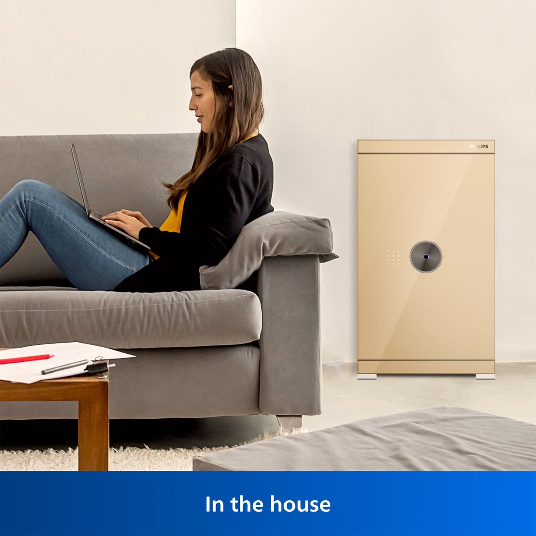Woman on a sofa using a laptop next to a gold smart safe